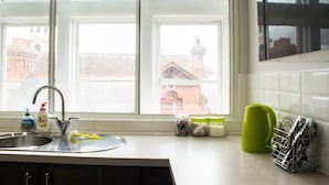 Una cocina con un lavabo, grifo y ventana. Hay frascos y una tetera verde en la encimera.