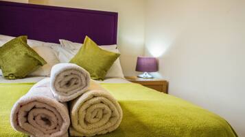 A neatly made bed with rolled towels, a green blanket, and two green pillows.