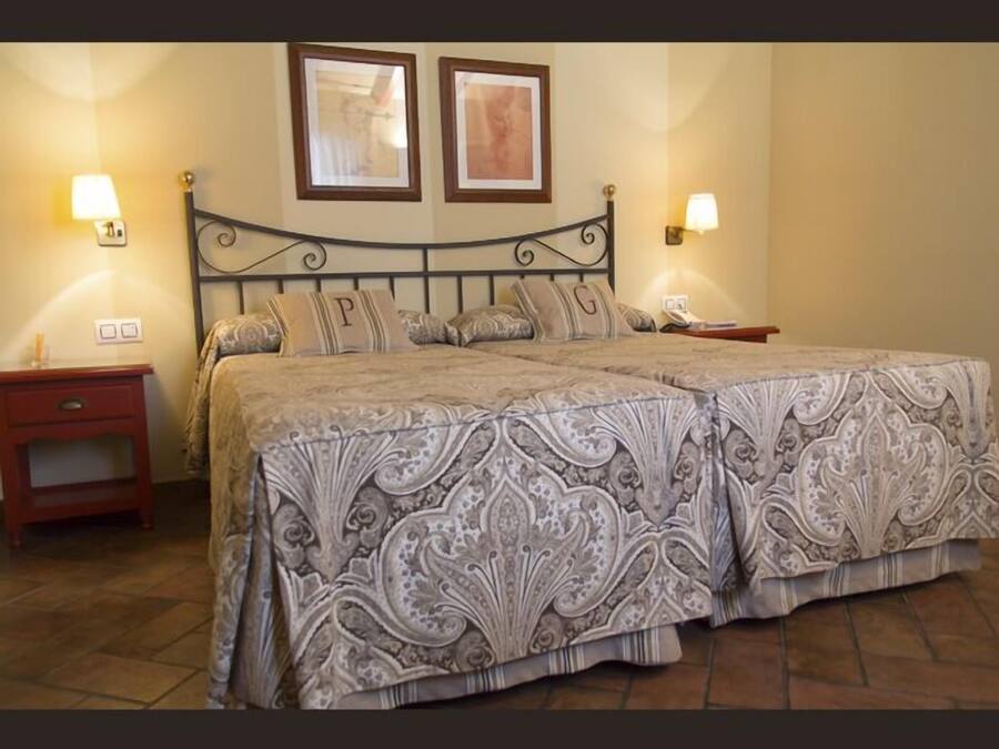 Una cama doble con colcha estampada, dos mesitas de noche y lámparas de pared.