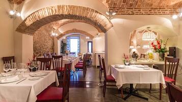 A restaurant with brick arches, white tablecloths, and red cushioned chairs.