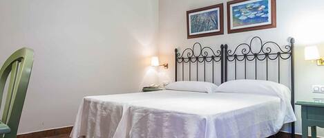 A single bed with a metal headboard, a nightstand with a lamp, and two framed pictures on the wall.