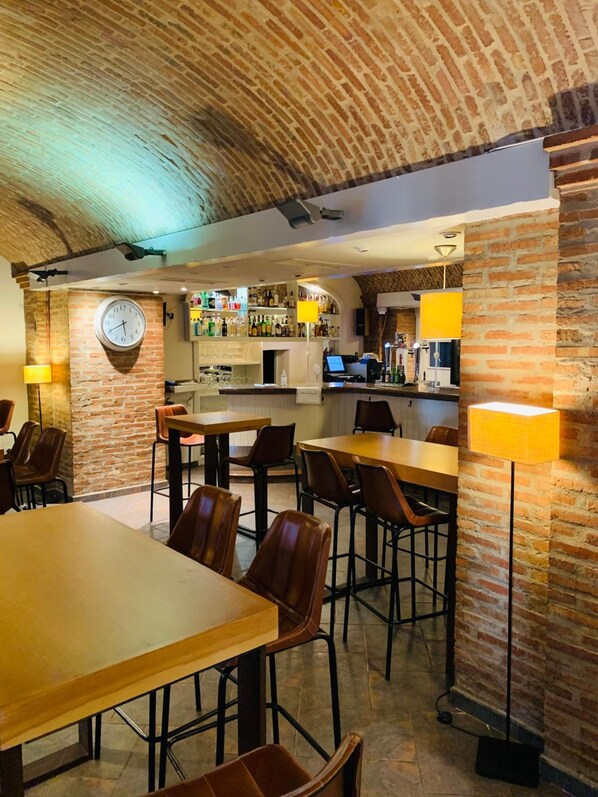 A restaurant with brick walls, wooden tables, and chairs. There is a clock on the wall and a bar area with bottles.
