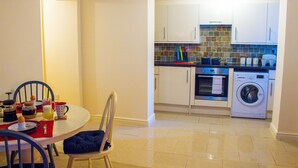 A compact kitchen with a dining area, including a table with chairs, a washing machine, an oven, and a tiled backsplash. - Hillbrook House Apartment 9 (Malvern)