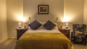 A neatly made bed with a yellow bedspread and two pillows, flanked by two bedside tables with lamps, a chair with a patterned cushion, and a framed picture on the wall. - Hillbrook House Apartment 9 (Malvern)