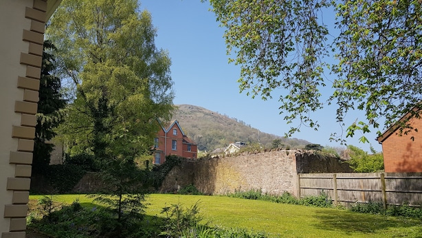 A red brick house with a stone wall and a wooden fence in a garden with green grass and plants. - Hillbrook House Apartment 9 (Malvern)