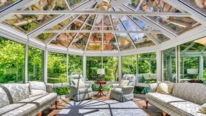 Een glazen orangerie, ingericht met banken en stoelen, en een centrale tafel.