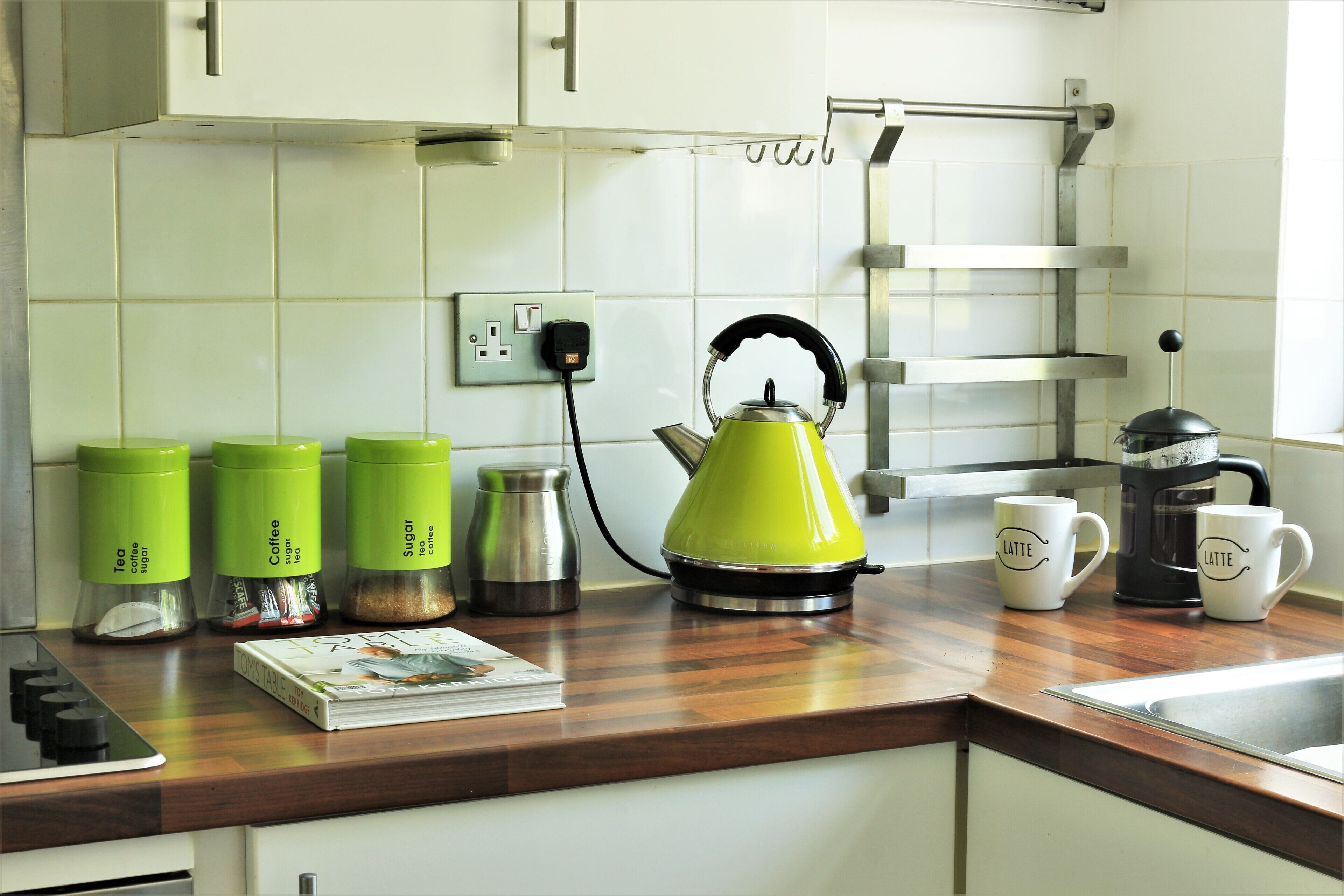 A kitchen with a wooden countertop, a kettle, coffee makers, and containers labeled for tea and sugar.