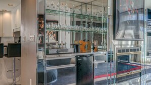 Un intérieur moderne avec une vitrine en verre contenant divers objets en verre, un réfrigérateur noir et un coin salon doté d’un sol à carreaux.