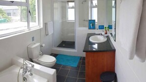 Et badeværelse med toilet, vask, bruser og badekar.