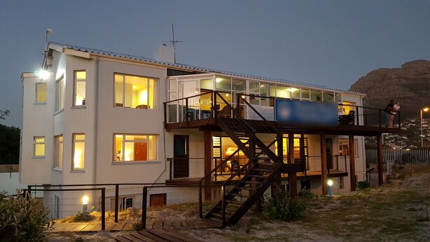 Et moderne hus med to etager, en balkon, en trappe og udsigt over det omkringliggende landskab.