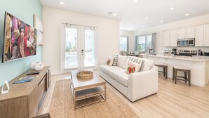 A modern living room with a sofa, coffee table, and a kitchen area with white cabinets and a microwave.