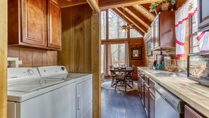 A cabin interior with wooden walls, a kitchen with a sink and stove, and a dining area with a table and chairs.