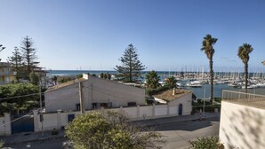 A coastal building with a flat roof, surrounded by trees and a marina with boats.