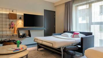 Een hotelkamer met een bed, een aan de muur bevestigde televisie, een bureau met stoel en een raam met gordijnen.