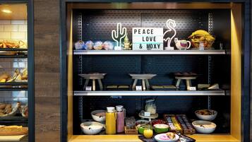 Een ontbijtbuffet met diverse gerechten en een bordje met de tekst 'Peace Love & Moxy'.