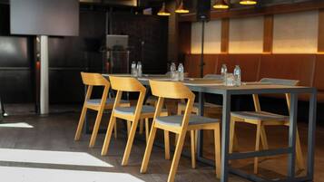 Un restaurante con sillas y mesas de madera, una pantalla grande e iluminación colgante.