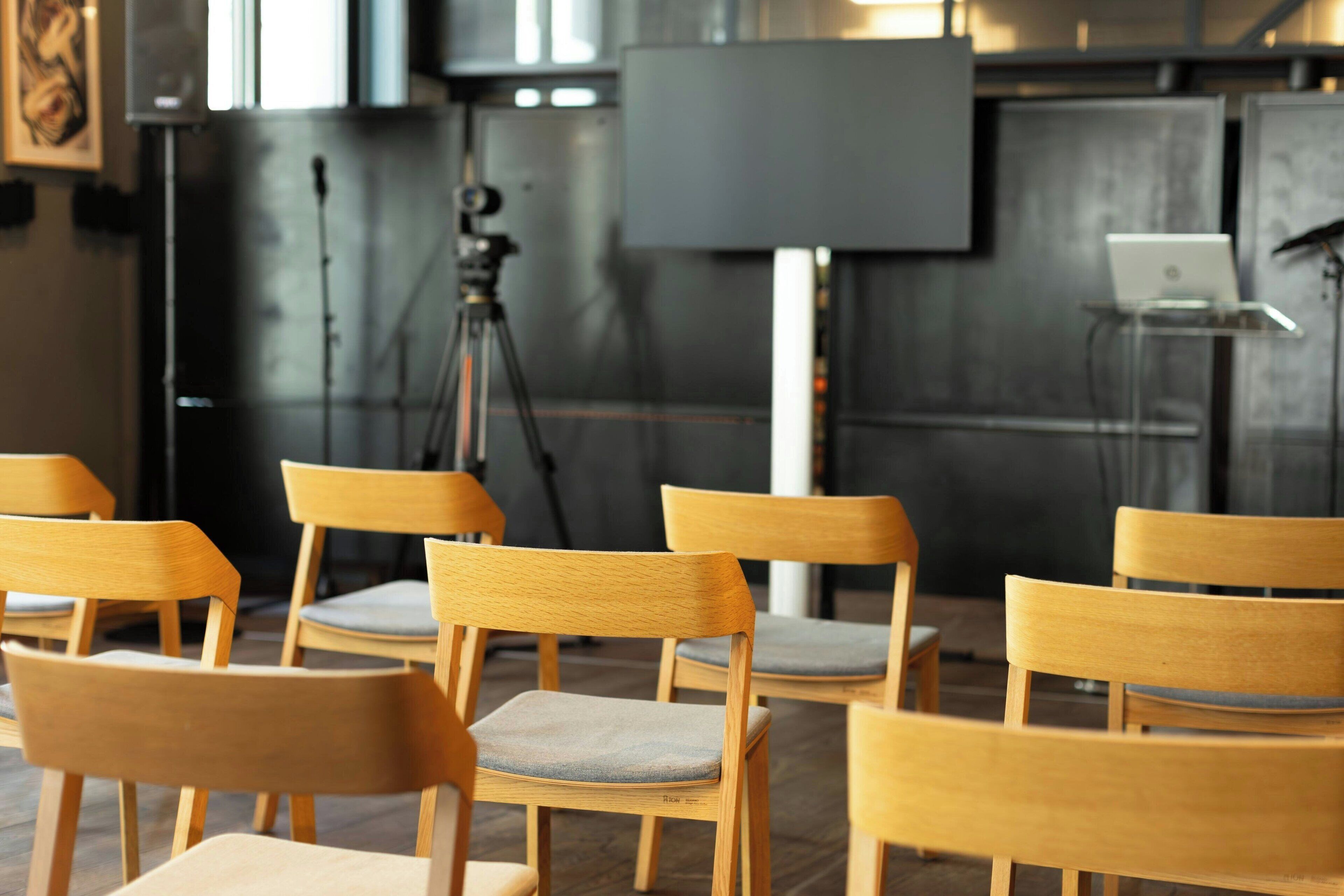 A conference room with wooden chairs, a tripod, and a laptop on a stand.