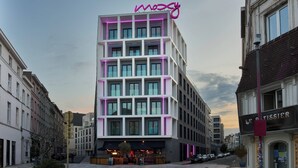 A modern building with a neon sign, a cafe, and a sign for 'Le Cuisinier'. - Moxy Brussels City Center (Brussels)