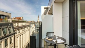 A modern balcony with a table and chairs, overlooking a cityscape with historic buildings and a church spire. - Moxy Brussels City Center (Brussels)