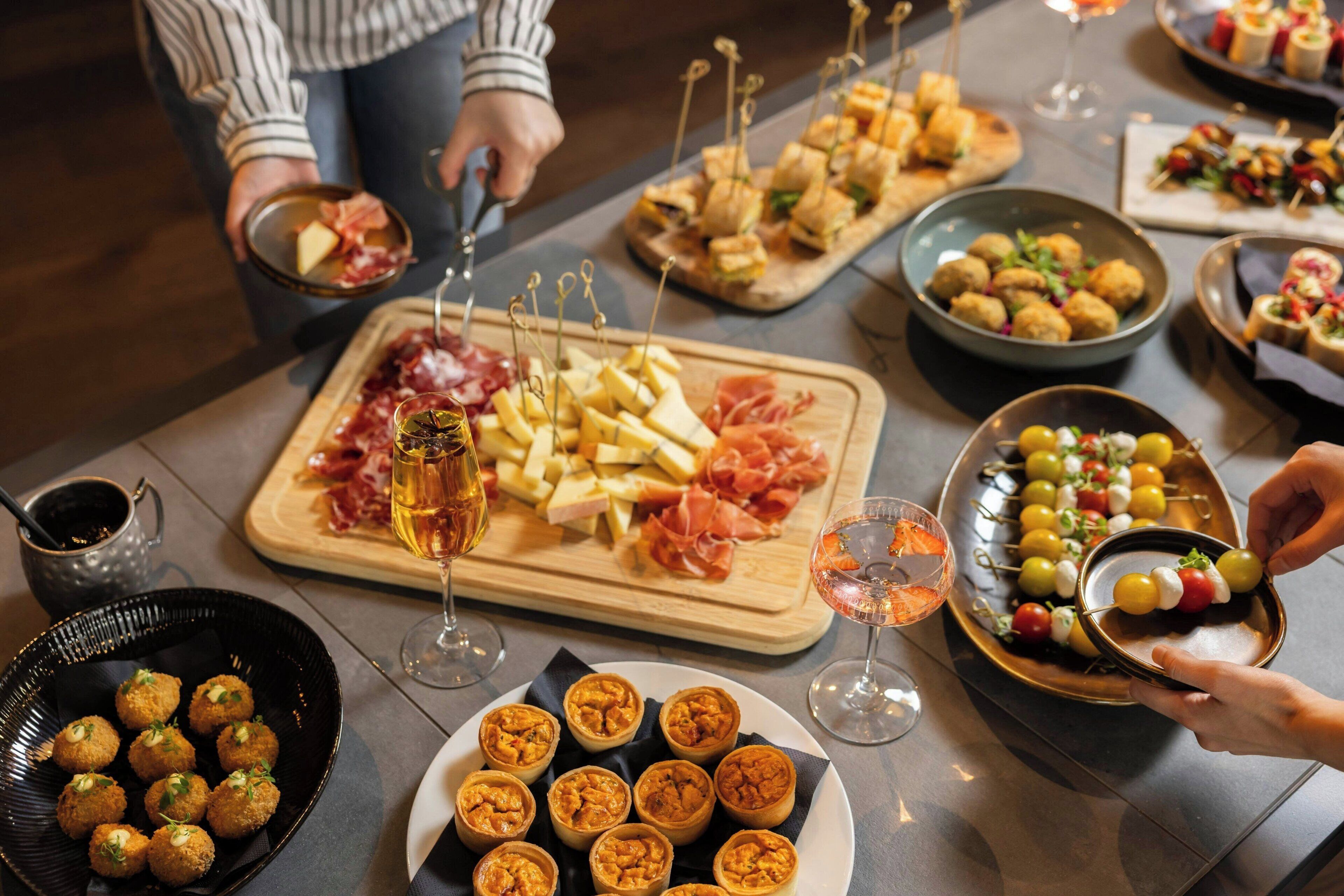Una mesa con diversos alimentos y bebidas, incluyendo queso, embutidos y aperitivos.