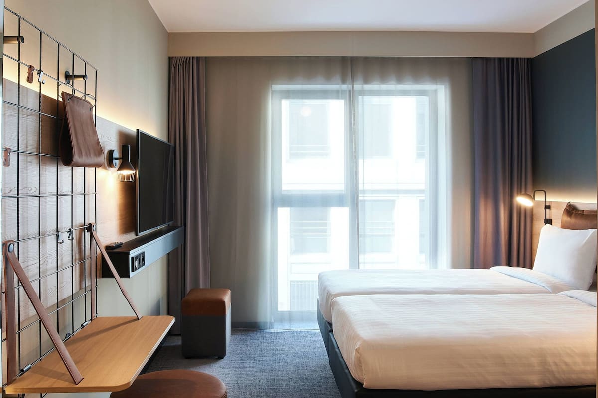 A hotel room with a bed, a TV mounted on the wall, a small table, and a bench.