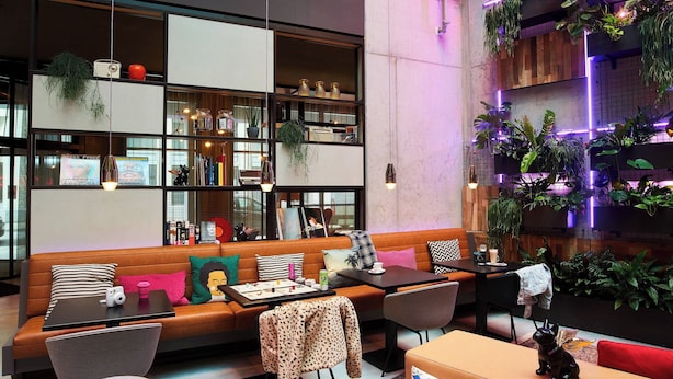 A modern lounge area with a sofa, chairs, a table, and a wall with plants. - Moxy Brussels City Center (Brussels)
