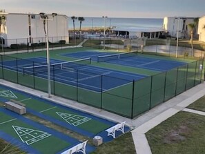 A tennis court with multiple courts, a seating area, and a view of the ocean.