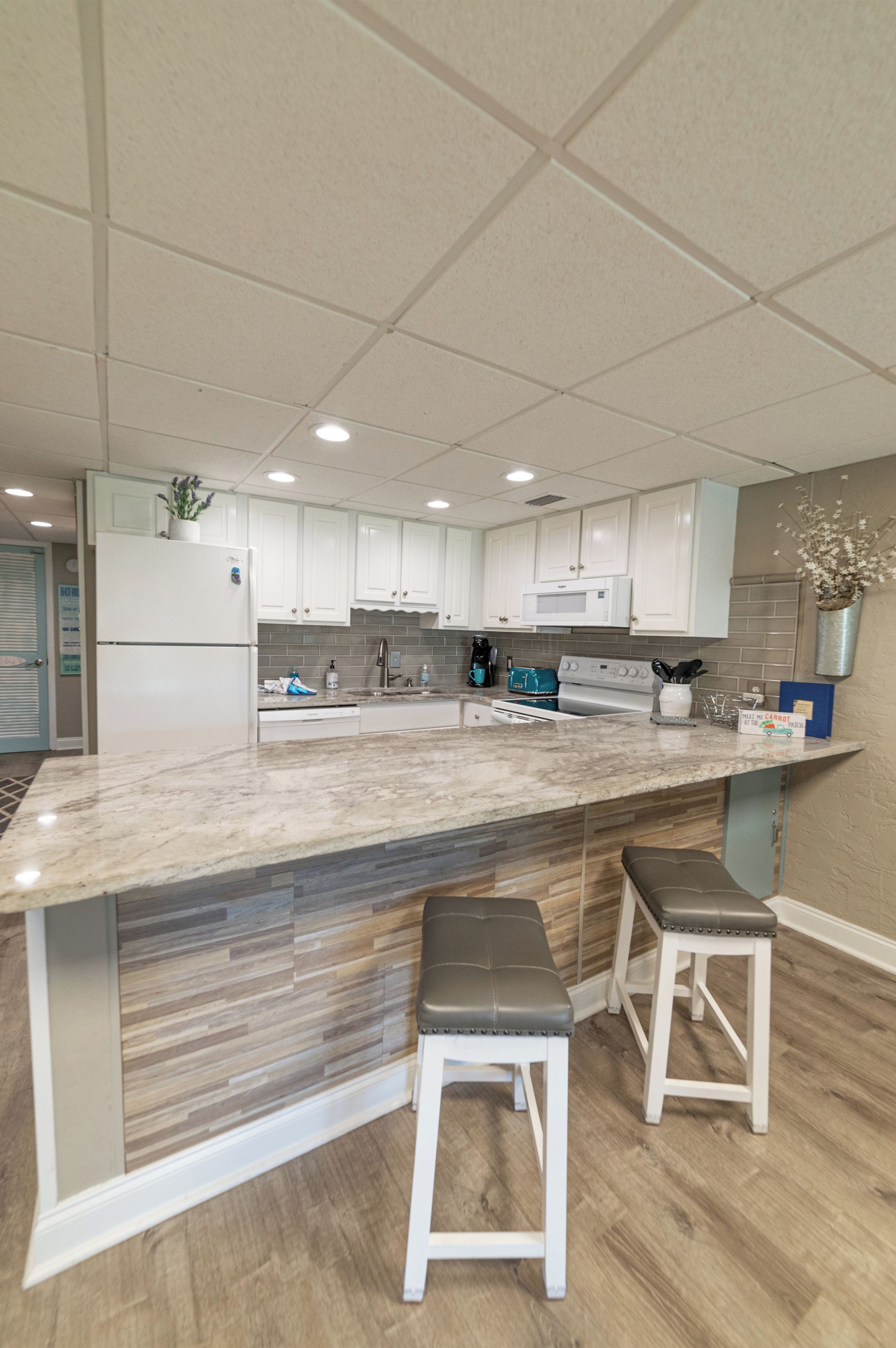 A modern kitchen with white cabinets, a marble countertop, and two bar stools.