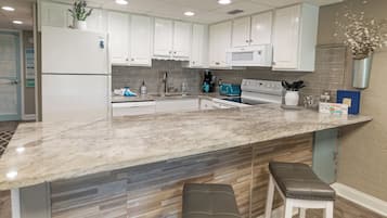 A modern kitchen with white cabinets, a marble countertop, and two bar stools.