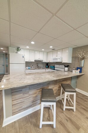 A modern kitchen with white cabinets, a marble countertop, and two bar stools.
