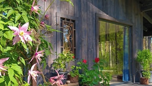 A rustic wooden building with large windows and a variety of potted plants and flowers in front. - Rabarberi LV #R2-Unique views at SeaSide Village (Saulkrasti)