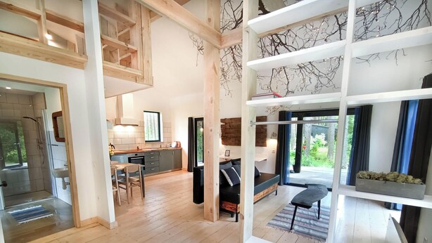 A spacious loft-style living area with a high ceiling, open-plan kitchen, and large windows offering views of the outdoors. - Rabarberi LV #R2-Unique views at SeaSide Village (Saulkrasti)