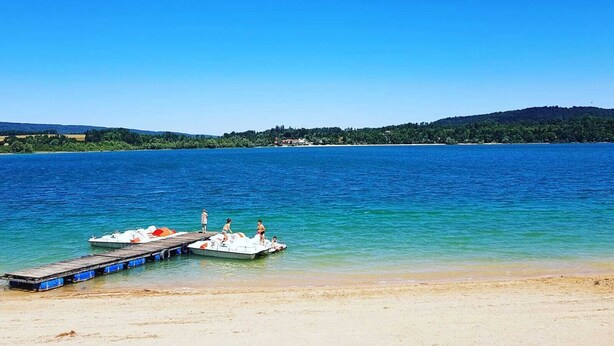 Um lago azul límpido com um cais de madeira e pequenos barcos.