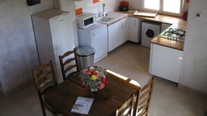 Uma cozinha compacta com geladeira, micro-ondas, pia e fogão. Há uma mesa de jantar com cadeiras e um vaso de flores.