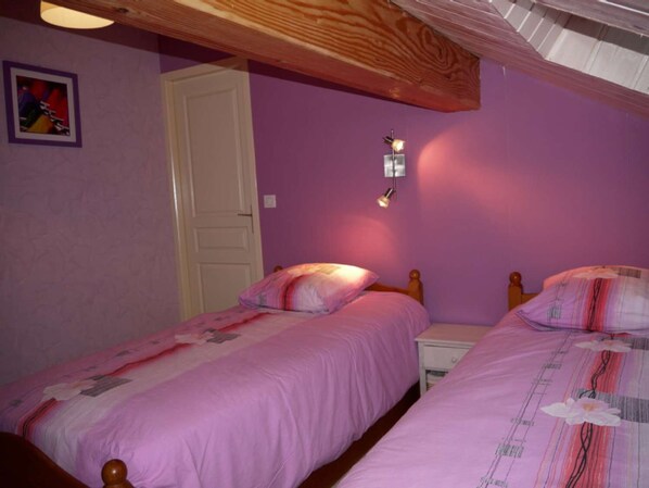 A bedroom with two single beds, a wooden ceiling, a white door, and a wall-mounted light fixture.
