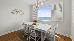 A dining area with a white table and chairs, a chandelier, and a window with white shutters overlooking a body of water. - Townhome with stunning view of Matlacha Pass (Matlacha)