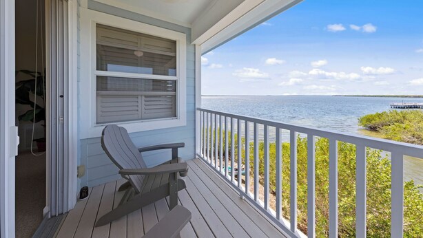 A wooden deck with a chair, a window with shutters, and a view of the water. - Townhome with stunning view of Matlacha Pass (Matlacha)