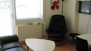 A room with a black leather sofa, a white table, a black armchair, and a floor lamp. - Plesners Anneks (Skagen)