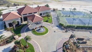 A modern building with a central courtyard, surrounded by a tennis court and a landscaped area with palm trees. - Modern 2-Bedroom Home with Pools in Noord (Noord)