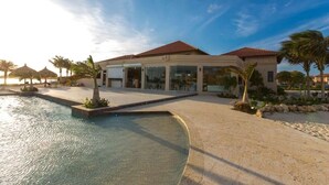 A resort with a swimming pool, palm trees, and a building with a red roof. - Modern 2-Bedroom Home with Pools in Noord (Noord)