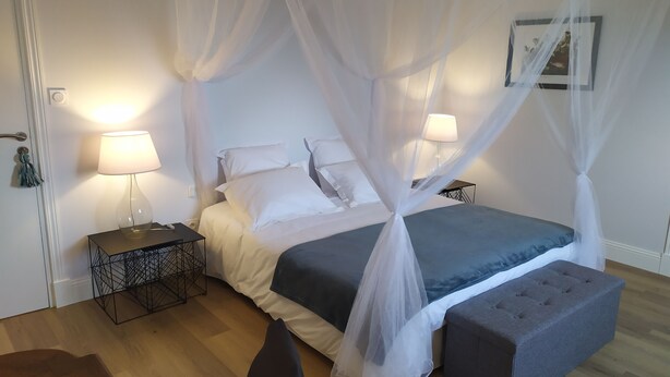 Un dormitorio con cama de dosel, mesitas de noche con lámparas, un banco y un cuadro en la pared.