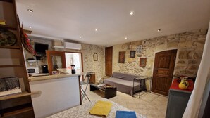 Un espacio habitable compacto con kitchenette, un sofá, una cama con ropa de cama estampada y una mesita con una toalla amarilla.