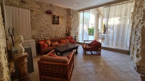 Una habitación con paredes de piedra, un sofá, una mesa de centro, sillas de mimbre y una escultura de busto.