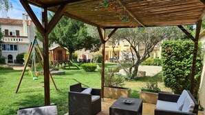 Un patio al aire libre con mobiliario de mimbre, un conjunto de columpios y vistas a un barrio residencial.
