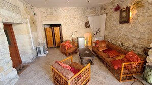 Una habitación acogedora con paredes de piedra, una puerta de madera, un sofá, un sillón de mimbre y una pequeña mesa.