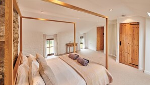 Ampia camera da letto con un grande letto, uno specchio con cornice in legno e vista su una porta e una finestra in legno.