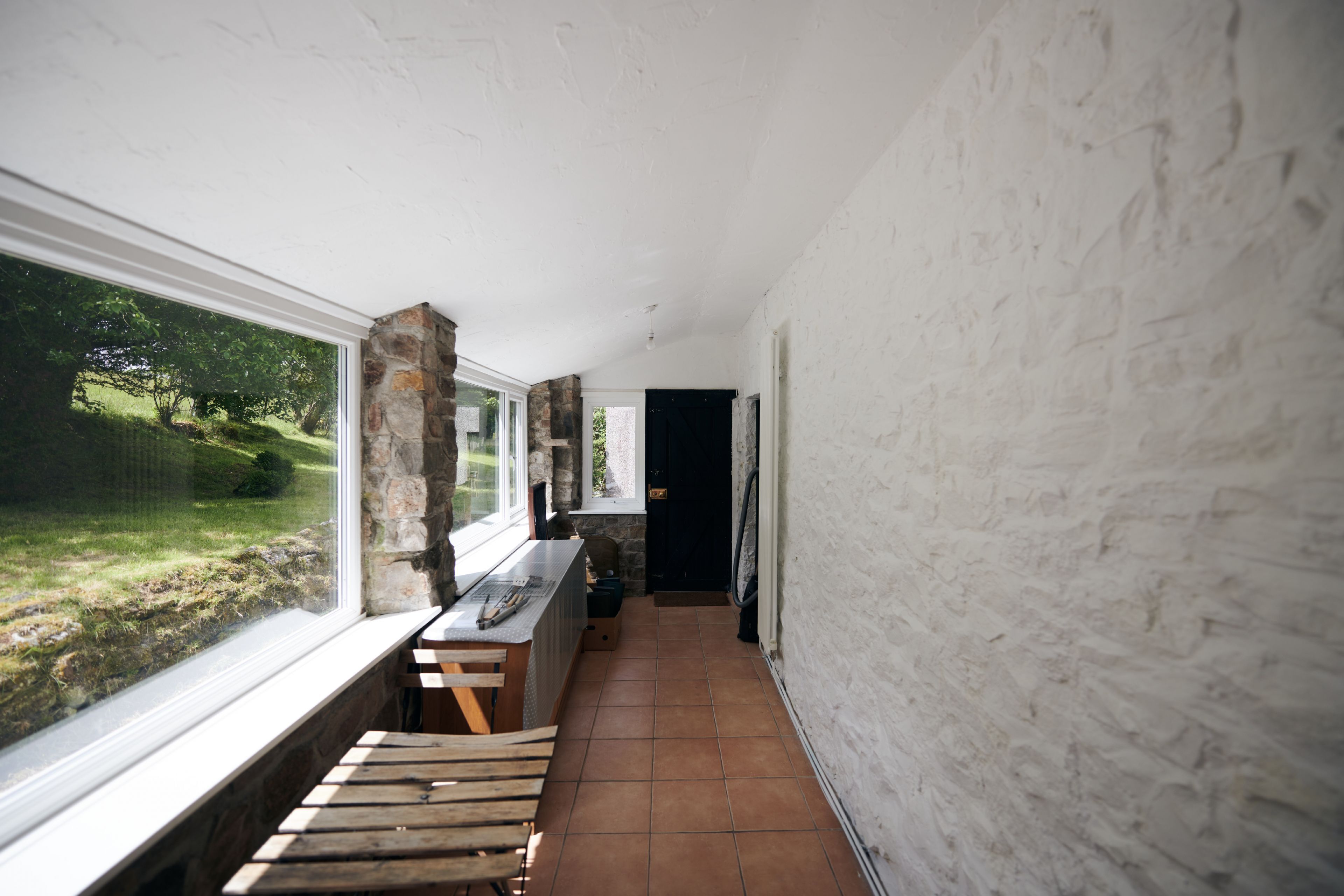 A narrow hallway with a wooden bench, a stone pillar, and a window overlooking a garden.