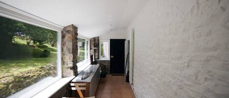 A narrow hallway with a wooden bench, a stone pillar, and a window overlooking a garden.