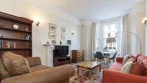 Ein Wohnzimmer mit Sofa, Couchtisch, Fernseher, Kamin und einem Essbereich mit Stühlen und Tisch.