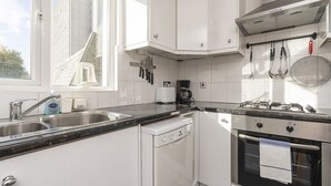 Eine moderne Küche mit weißen Schränken, einem Geschirrspüler, einem Backofen und einem Fenster mit Blick auf ein Backsteingebäude.